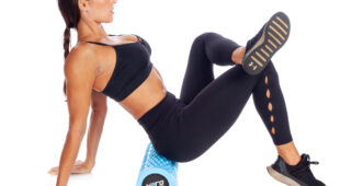 female athlete wearing a black sports bra and black leggings while doing a lower body stretch on a blue hero strength foam roller