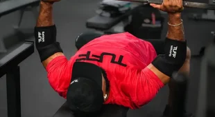 image of a man doing a bench press wearing the Tuff Wraps 5mm elbow sleeves in all black colorway